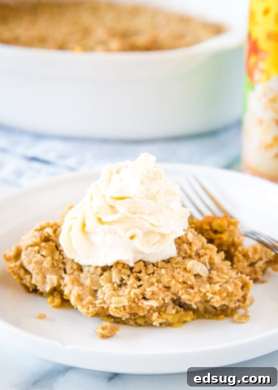 A perfectly portioned slice of pumpkin crisp on a white plate, beautifully topped with a swirl of whipped cream.
