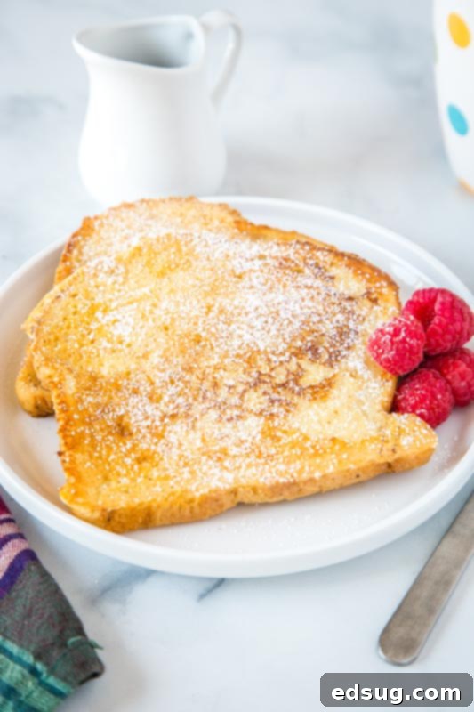 Golden Sourdough French Toast 6 A stack of two sourdough french toast slices on a white plate, dusted with powdered sugar, ready to be served.