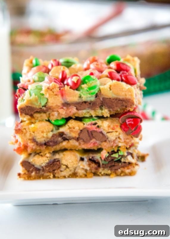 Yuletide Magic Cookie Bars 2 christmas magic bars stacked on white plate, showing the distinct layers of chocolate, peanut butter chips, coconut, and M&M's