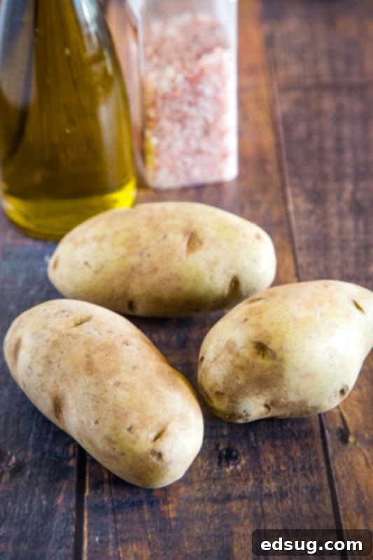 Crispy Air Fryer Baked Potato 3 potatoes on table with olive oil and salt behind them.