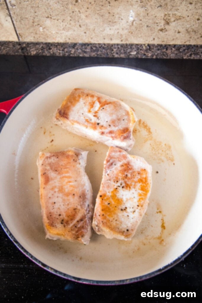 Effortlessly Perfect Sous Vide Pork Chops 5 Thick-cut sous vide pork chops browning intensely in a hot cast iron skillet during the searing process.