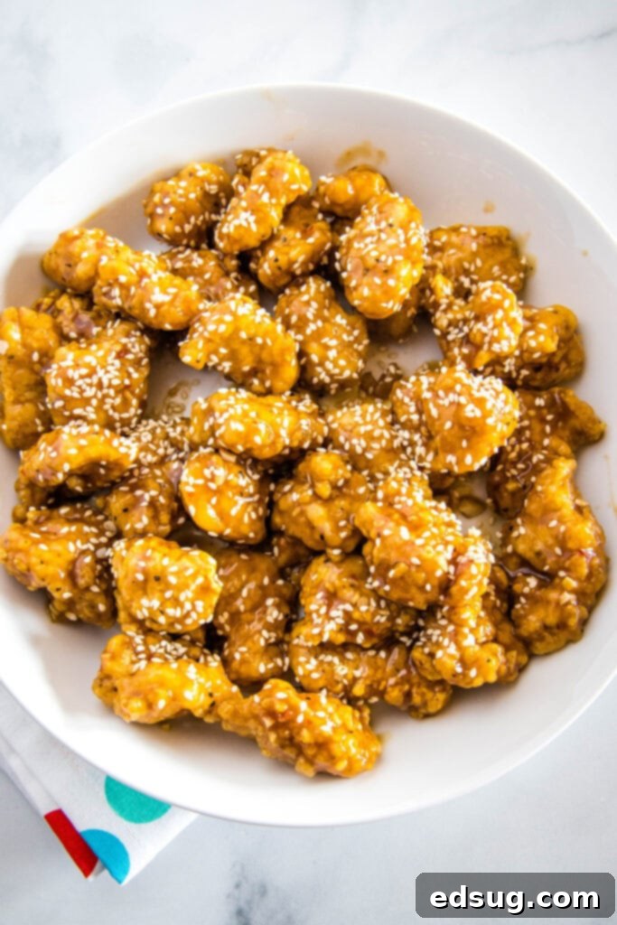 Effortless Sesame Chicken 6 A freshly cooked serving of sesame chicken, glistening with sauce, resting on a white plate.