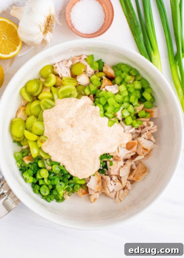Diced chicken, halved grapes, and chopped vegetables mixed in a large bowl, ready for the dressing.