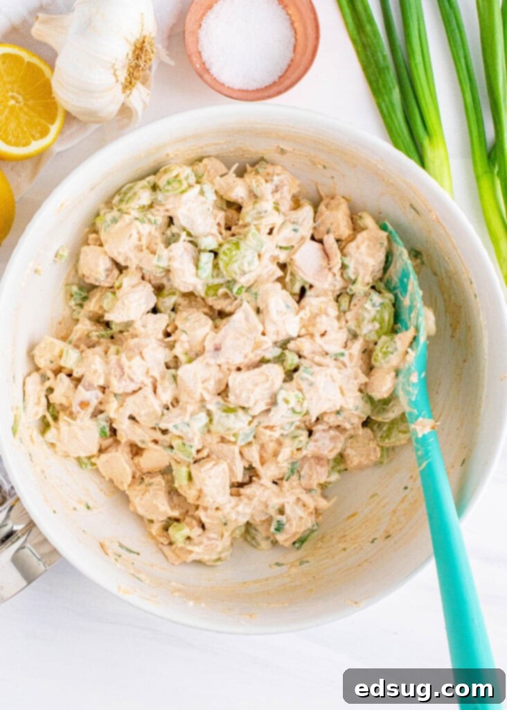 Creamy chicken salad with grapes being mixed in a glass bowl, showcasing its rich texture.
