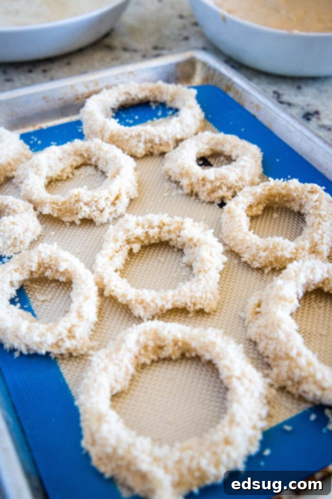 Crispy Air Fryer Onion Rings 4 Coated onion rings neatly arranged on a baking sheet before refrigeration.