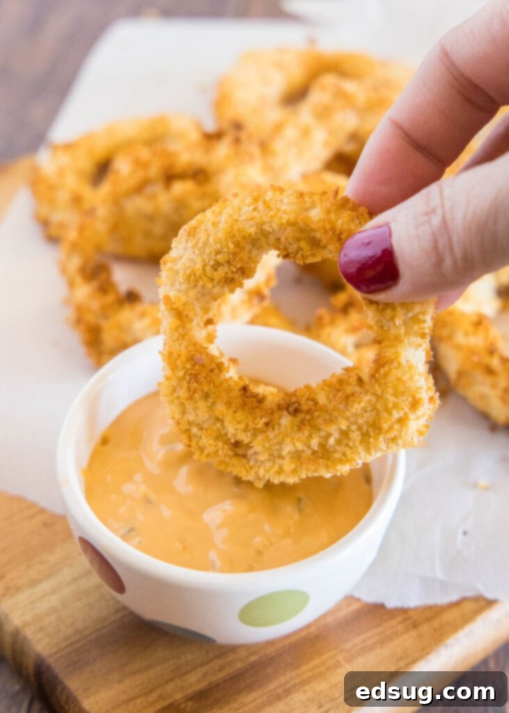 Crispy Air Fryer Onion Rings 6 A single air-fried onion ring being dipped into a creamy sauce.
