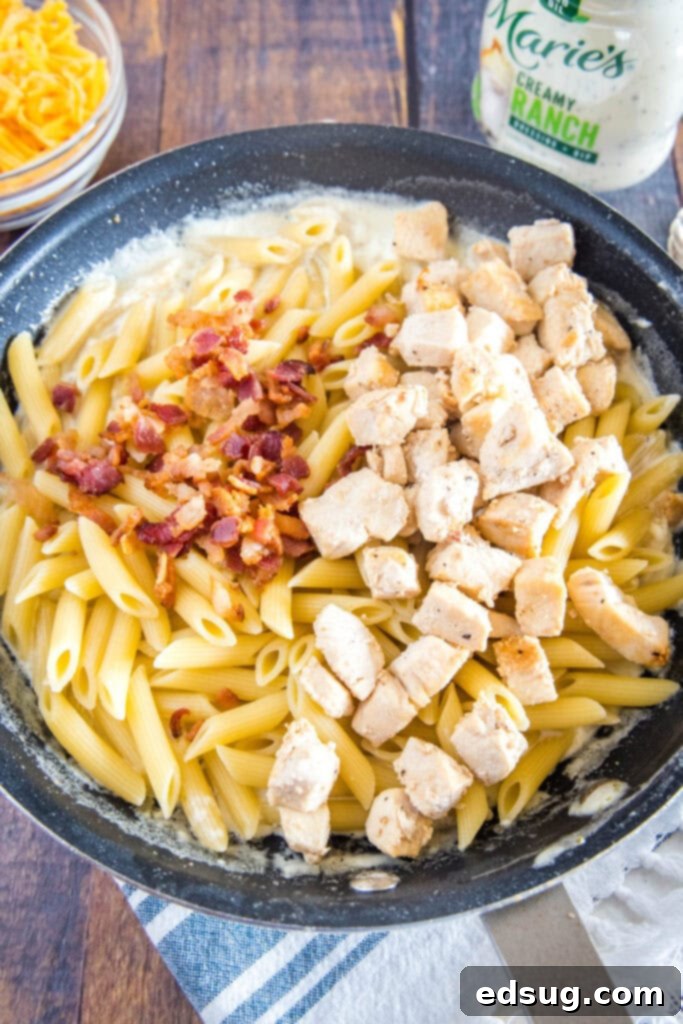 Creamy Chicken Bacon Ranch Pasta 5 Adding cooked chicken, pasta, and bacon to the creamy ranch sauce in a skillet