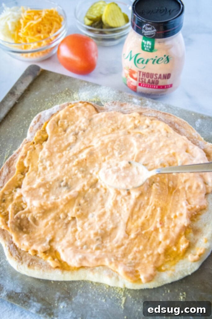 Loaded Burger Pie 4 Thousand Island dressing being spread evenly over the pizza crust before adding other toppings.