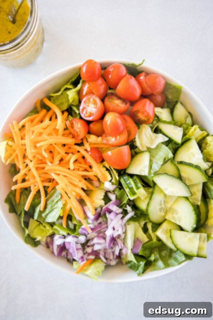 A vibrant green salad in a bowl, topped with a colorful array of fresh vegetables like shredded carrots, cucumbers, and tomatoes.
