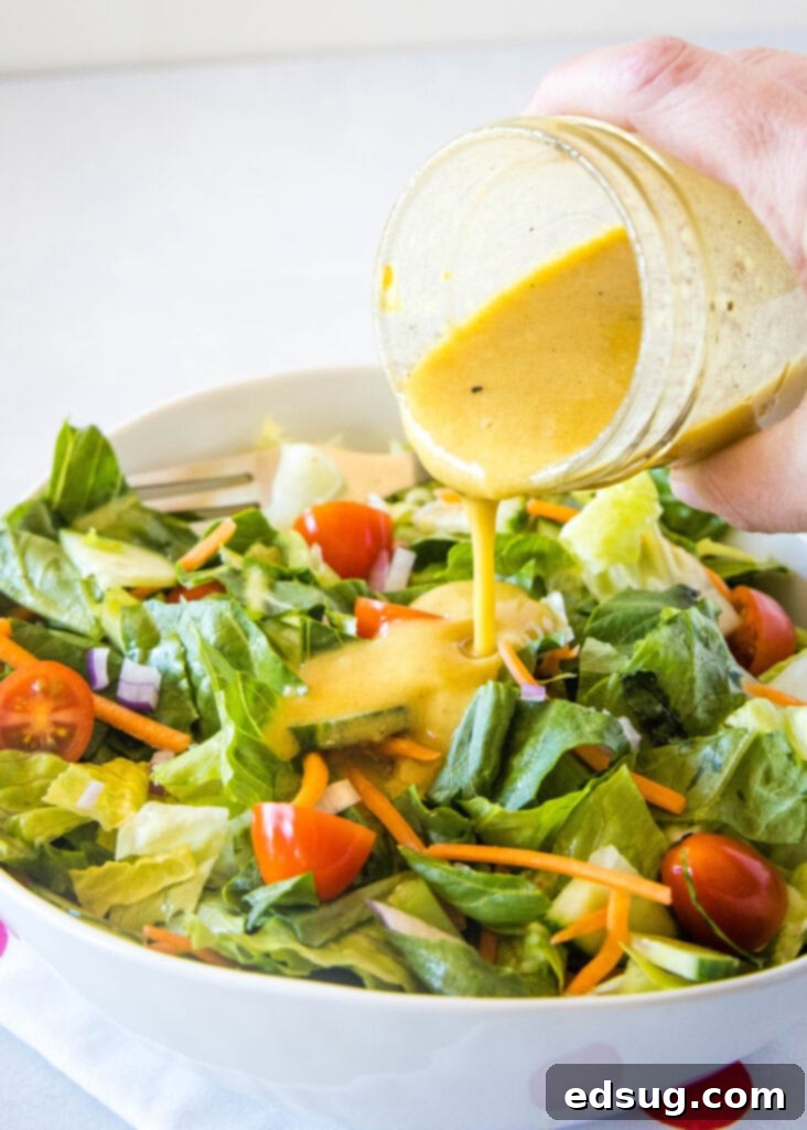 Homemade Dijon vinaigrette being poured over a fresh green salad with various vegetables.