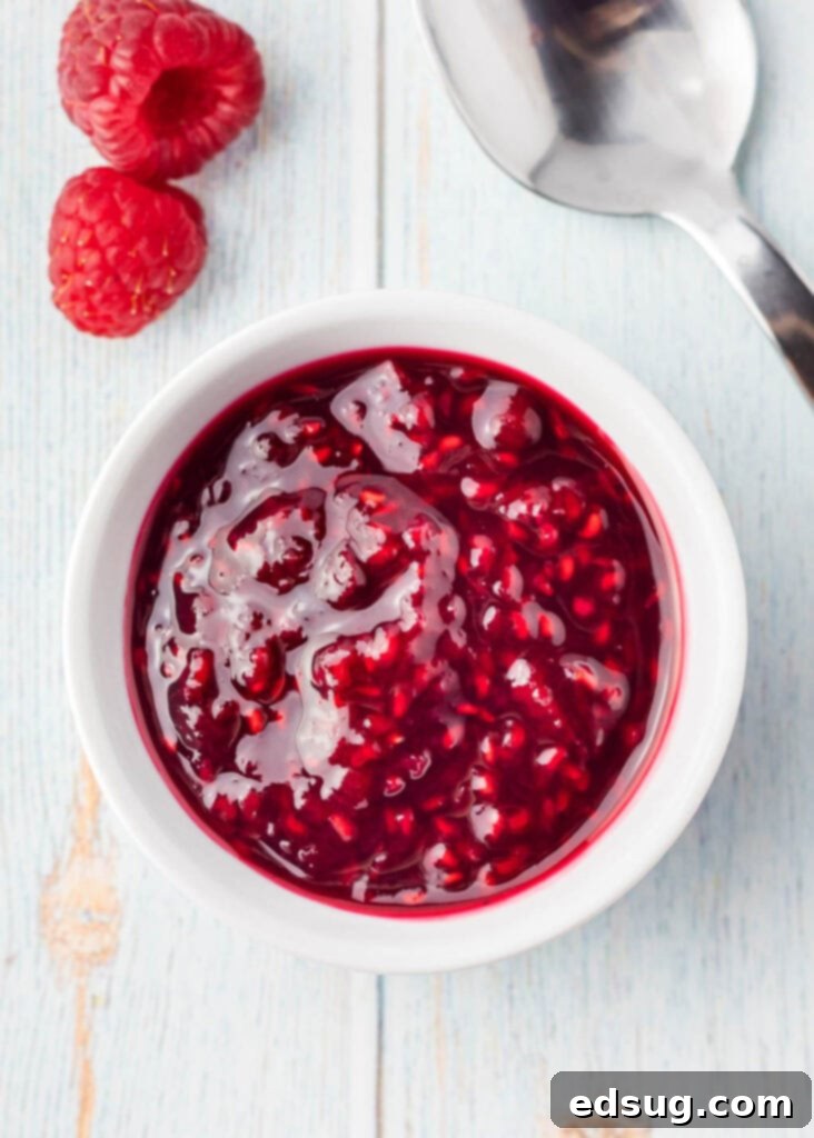Effortless Raspberry Sauce 5 A small bowl filled with homemade raspberry sauce, garnished with fresh raspberries, ready to be served.