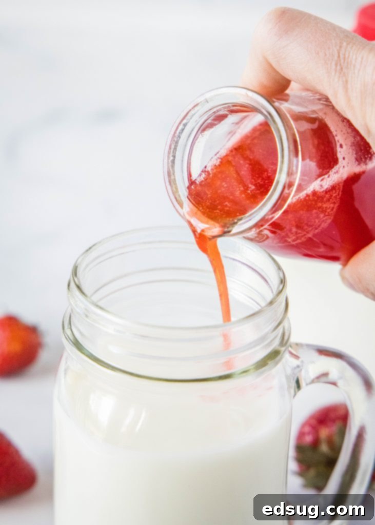 hands pouring vibrant homemade strawberry syrup into a glass of cold milk, creating a delicious drink