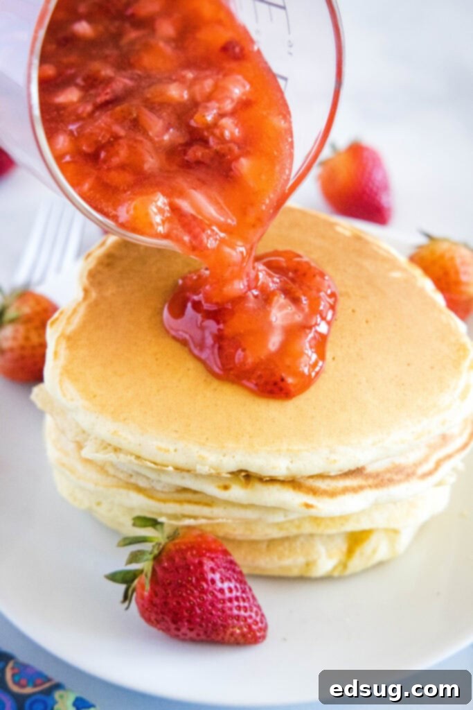 Pouring homemade strawberry syrup over a stack of fluffy pancakes, highlighting its rich texture and fresh berries.