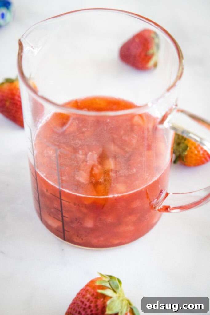 Freshly made strawberry syrup in a clear measuring cup, showing its vibrant red color and slight thickness.