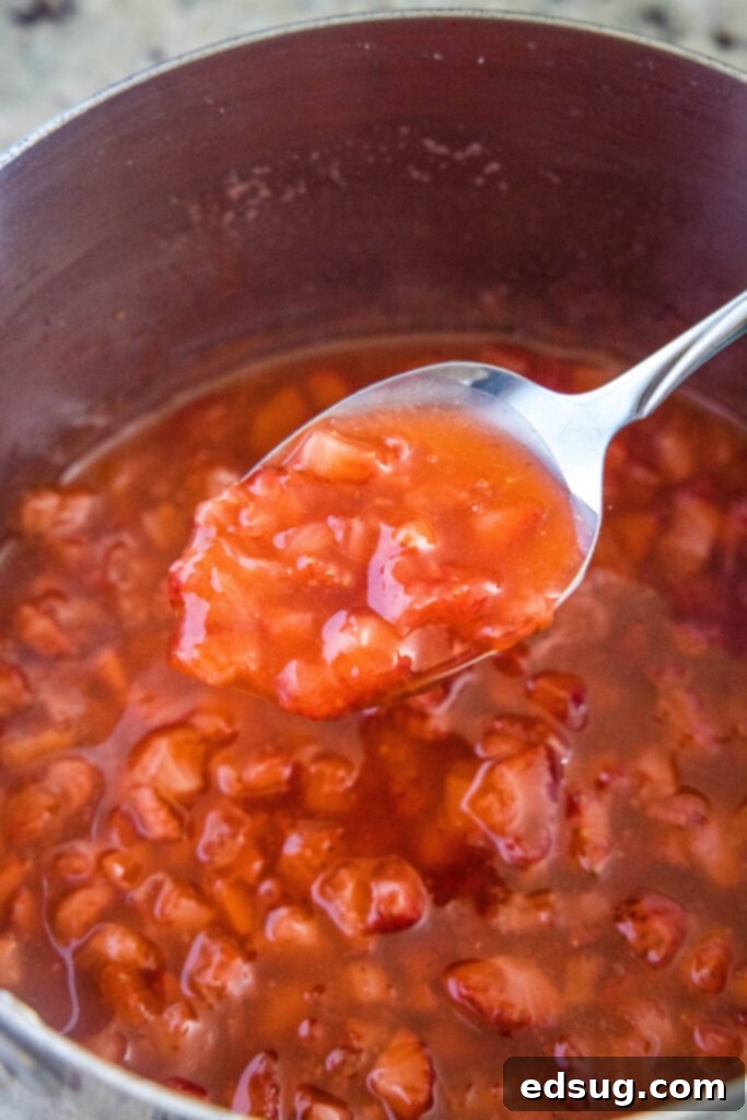 A spoonful of cooked strawberry syrup showing its thickness and chunks of fruit.
