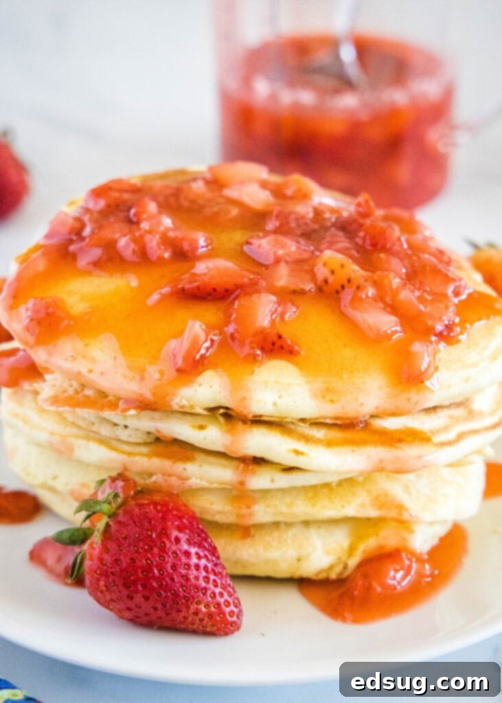 A stack of golden pancakes generously topped with homemade strawberry syrup and fresh strawberry slices.
