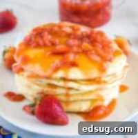 Close up stack of pancakes with strawberry sauce, ready to be enjoyed.