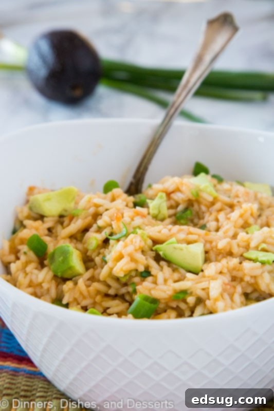 A bowl of fluffy Mexican rice with vibrant green avocado chunks and fresh scallions, ready to be served.