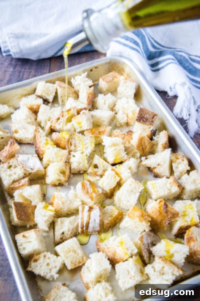 Crispy Homemade Croutons 4 A hand drizzling olive oil over bread cubes spread out on a baking tray