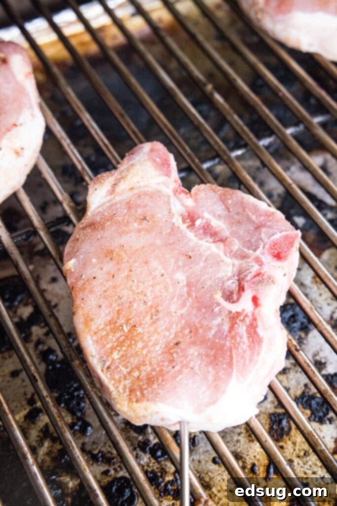 Succulent Smoked Pork Chops 4 Cooked pork chops on a smoker grill grate, showing perfect sear and smoke color.