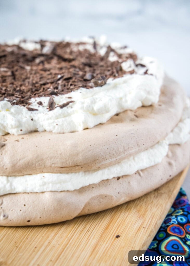 chocolate pavlova on a cutting board topped with whipped cream and chocolate shavings
