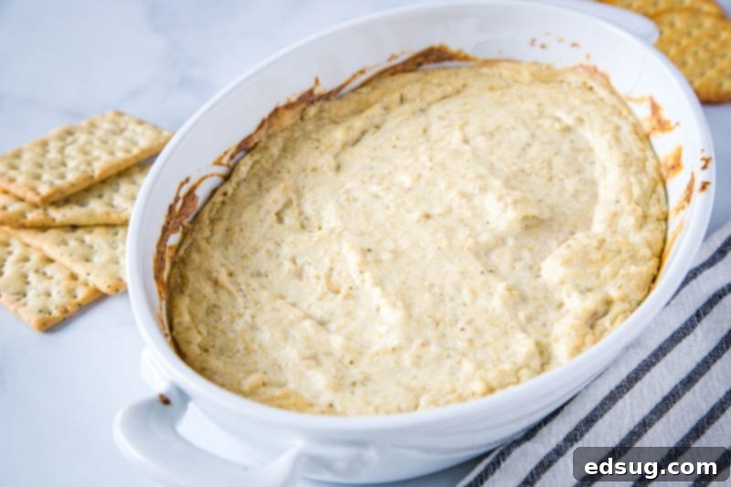 Hot artichoke dip served in a rustic bowl, surrounded by an assortment of dippers including crackers, toasted bread, and fresh vegetables, ready for a party.