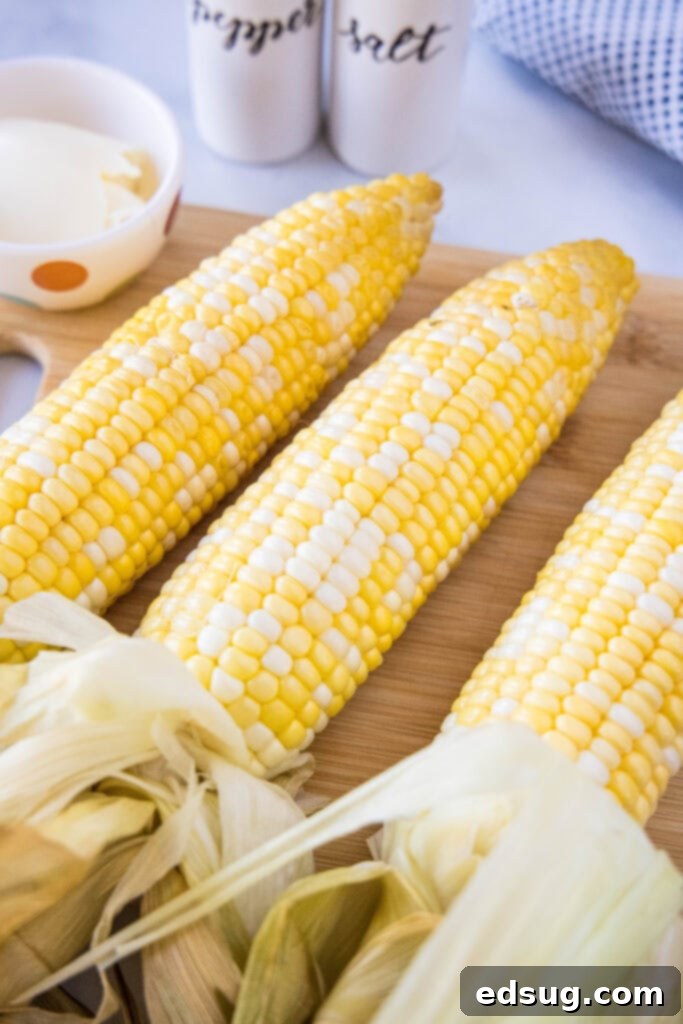 Three ears of fresh corn on a cutting board, ready for preparation.