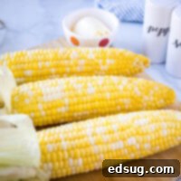 Close-up of perfectly smoked corn on the cob on a cutting board, garnished with butter and herbs.