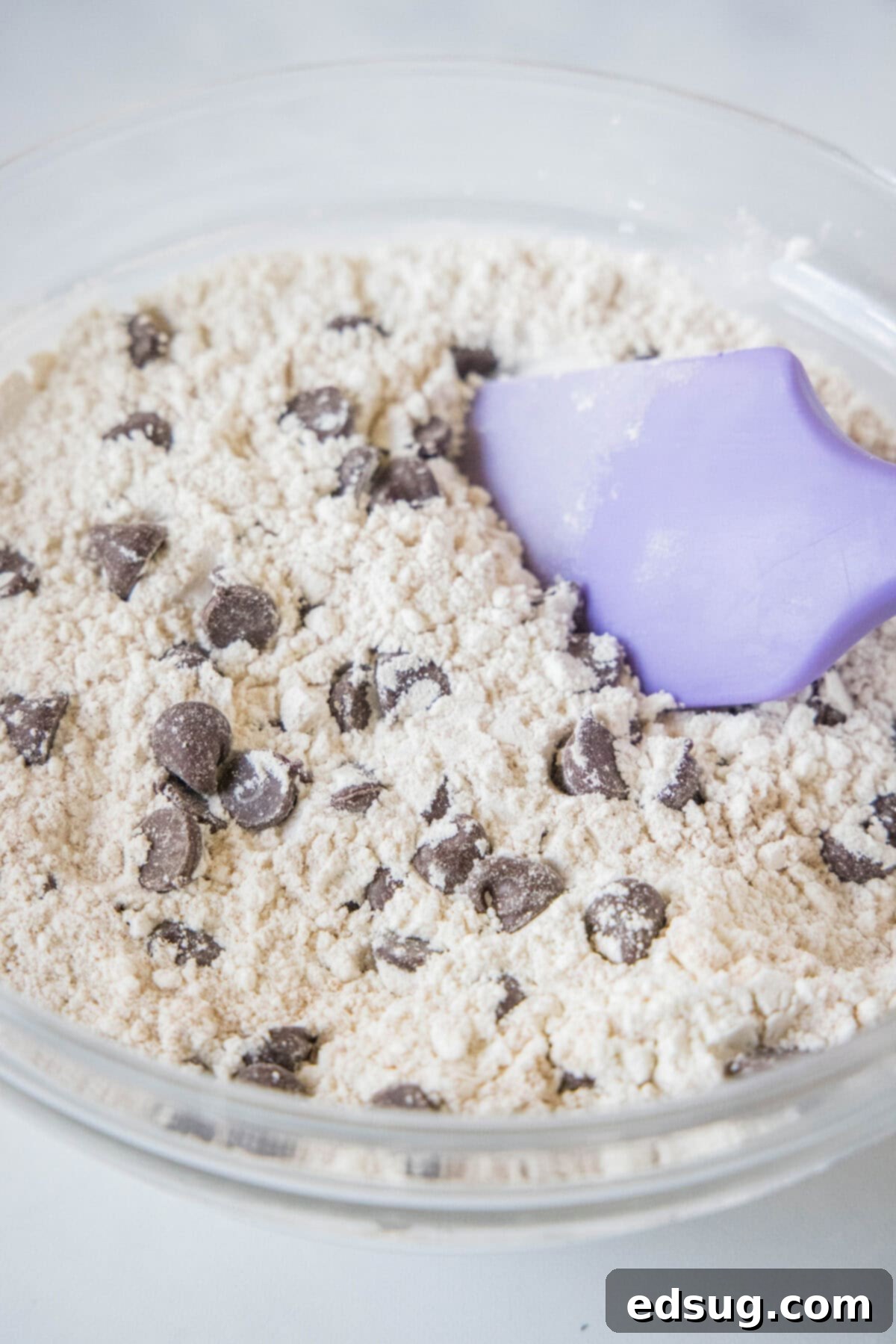 Chocolate chips folded into dry muffin ingredients in a glass bowl with a rubber spatula.