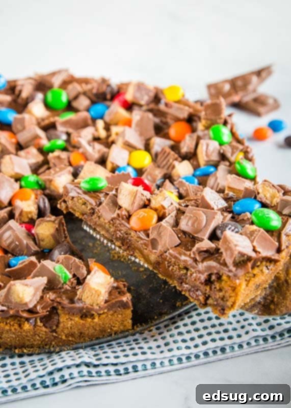 Decadent Chocolate Cookie Pizza 4 A vibrant dessert pizza, made from a large chocolate chip cookie base, adorned with a variety of colorful and chocolate candies and a light frosting, resting on a rustic wooden surface ready to be enjoyed