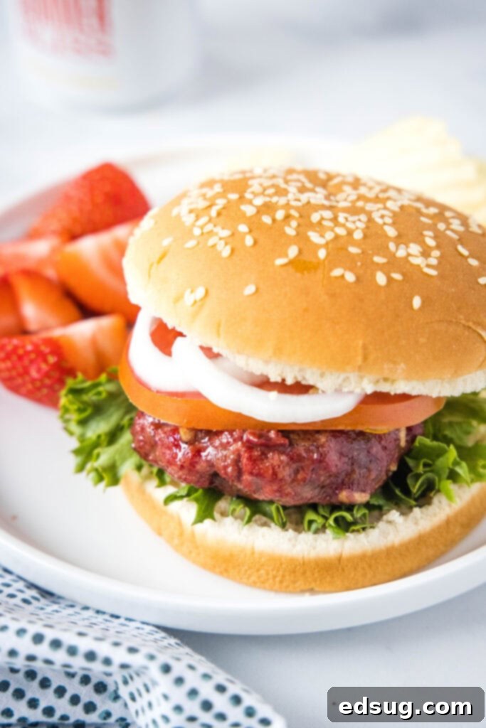looking down on a plate with a smoked hamburger on a bun with a plate of strawberries