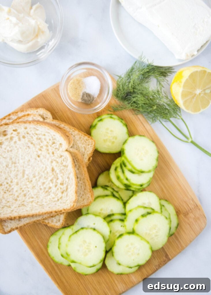 Cucumber Sandwiches 3 A cutting board with fresh ingredients laid out: white bread, English cucumber, a bowl of cream cheese spread, and fresh dill.