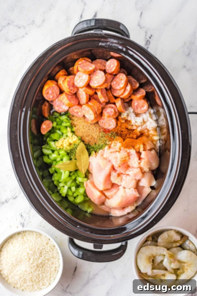 Effortless Slow Cooker Jambalaya 4 Raw ingredients for Jambalaya, including chicken, sausage, bell pepper, and tomatoes, placed inside a crock pot, ready for slow cooking.