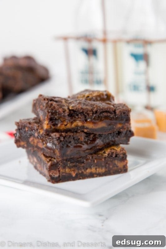 Stack of rich chocolate caramel brownie bars on a white plate, showcasing gooey caramel.