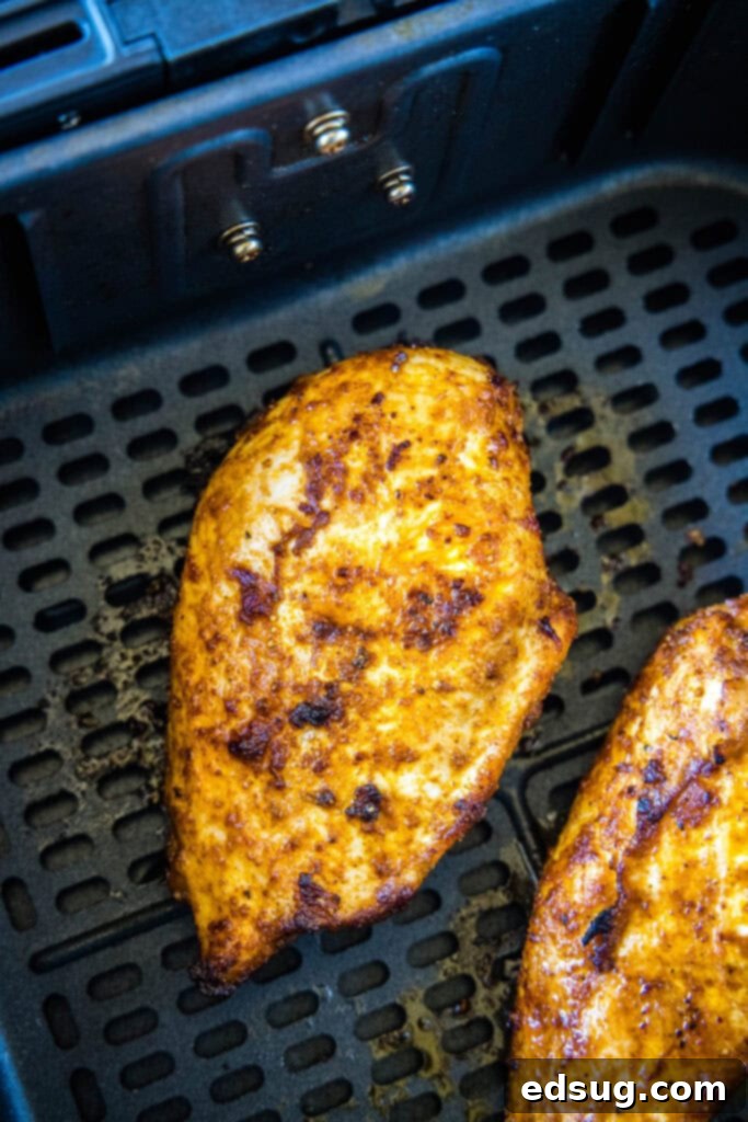 Raw seasoned chicken breasts cooking inside an air fryer basket, showing the even heat distribution