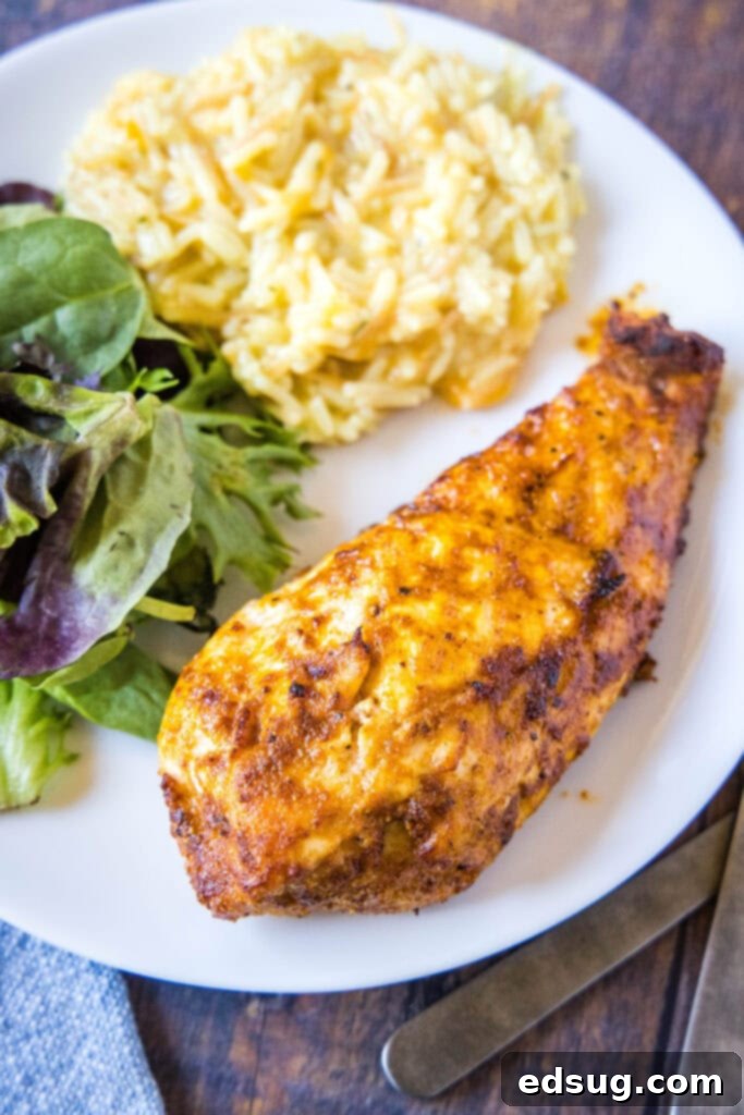 A perfectly cooked air fryer chicken breast on a plate with a side salad and rice, ready to eat