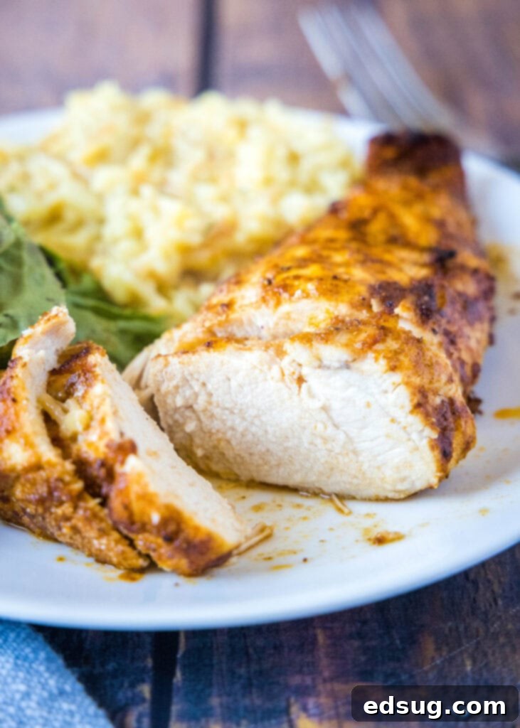 Close-up of perfectly cooked, sliced air fryer chicken breast on a plate with blurred salad and rice in the background