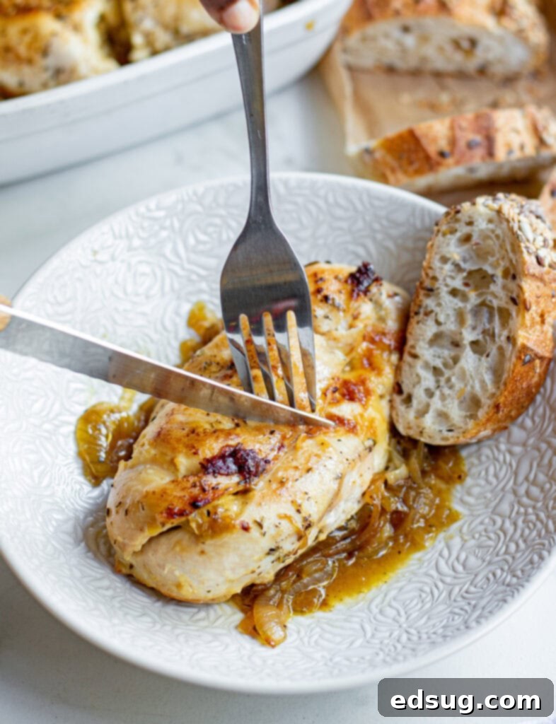 Creamy French Onion Chicken 5 piece of chicken with caramelized onions on a white plate with a knife cutting into it