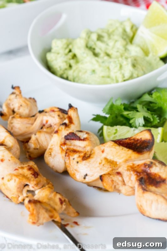 Zesty Chicken Kebabs 2 grilled chicken on skewers with avocado dipping sauce on a plate