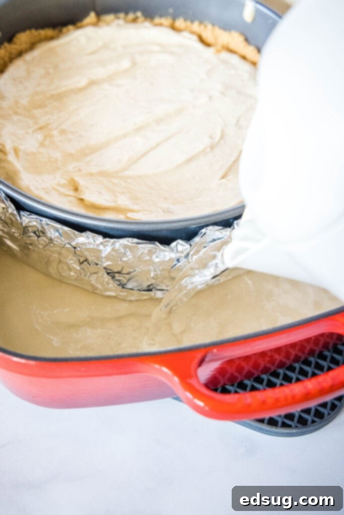 A springform pan with cheesecake filling being placed into a roasting pan for a water bath before baking.