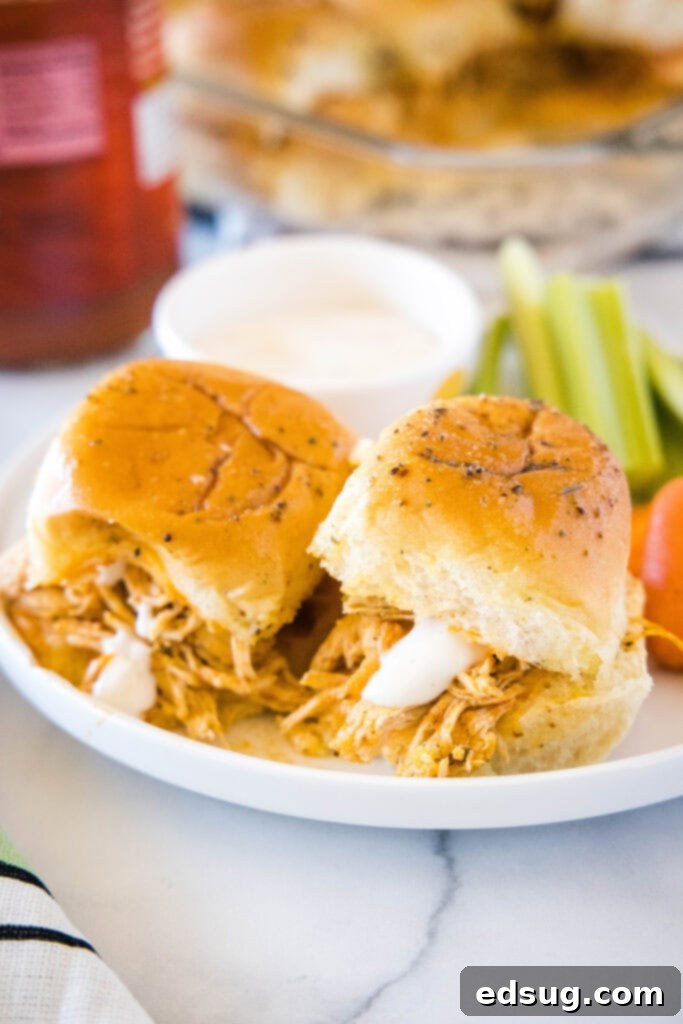 Two buffalo chicken sliders on a white plate with carrots and celery in the background, ready to be served as a delicious appetizer or meal