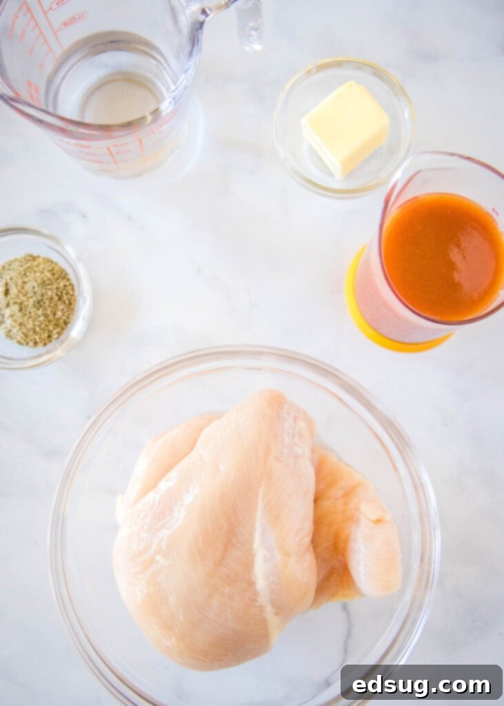 Ingredients laid out on a counter, including chicken breasts, buffalo sauce, butter, ranch seasoning, and water, ready to make buffalo chicken sliders