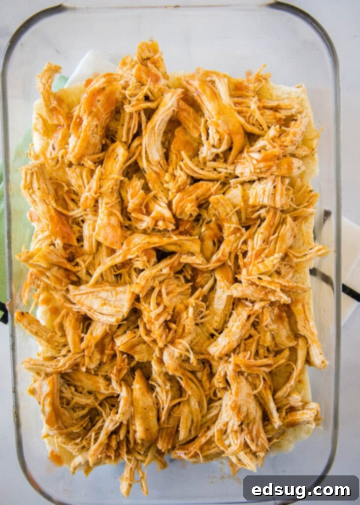 Buffalo chicken filling spread evenly over slider buns in a baking dish, ready for the top buns to be placed and baked