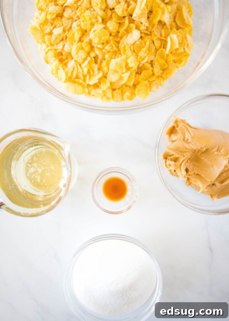 A selection of cornflake cookie ingredients laid out on a clean surface: cornflakes, peanut butter, sugar, corn syrup, and vanilla extract.