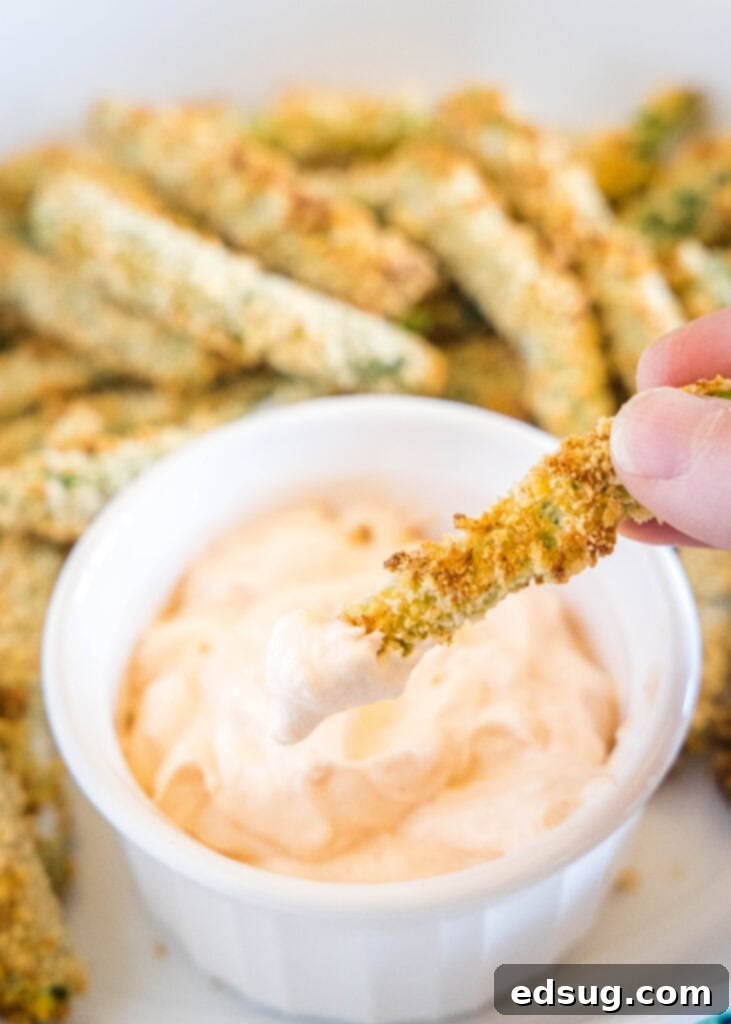 Hand dipping an air fryer green bean fry into a bowl of spicy mayo