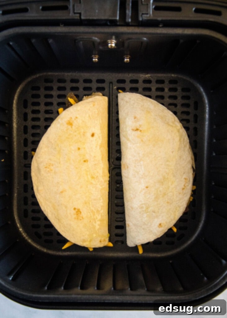 A pair of neatly folded, oil-brushed quesadillas resting in an air fryer basket, perfectly positioned and ready for cooking to achieve a golden, crispy finish.