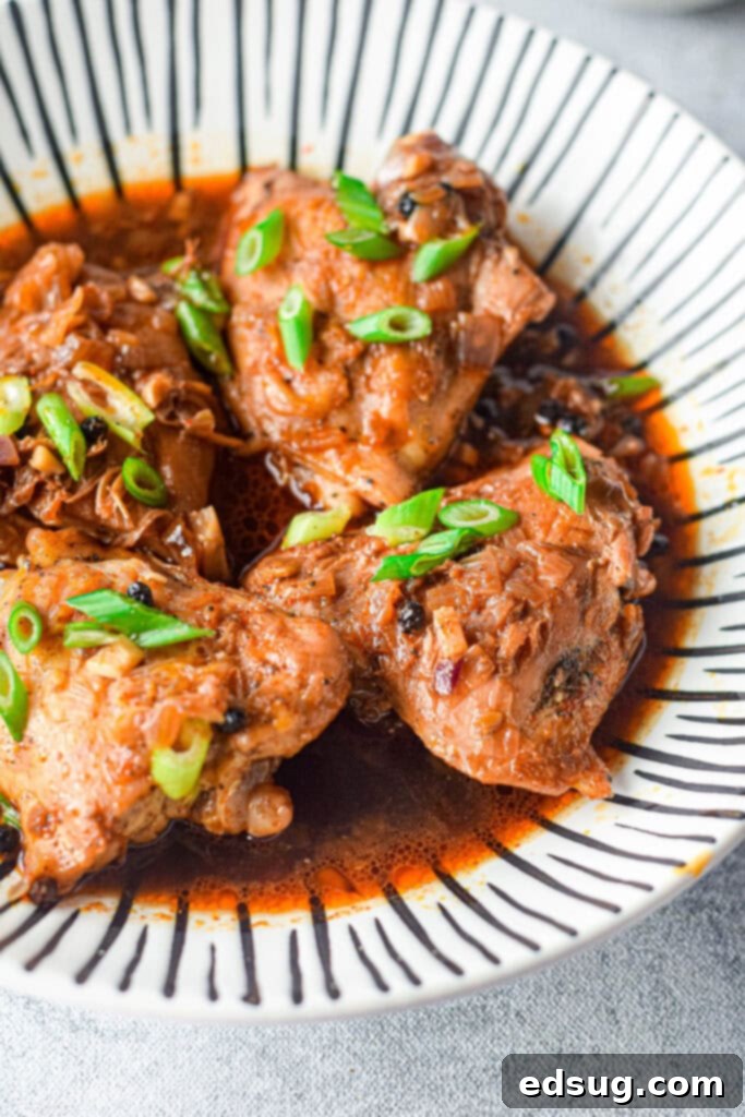 A vibrant plate of Filipino Instant Pot Chicken Adobo with tender chicken thighs, bay leaves, and peppercorns, served over steamed white rice.