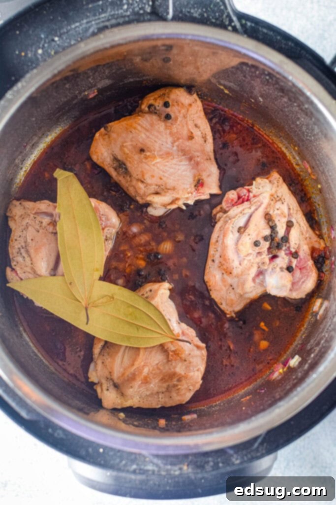 Chicken thighs simmering in the Instant Pot during the sauce thickening stage for Instant Pot Chicken Adobo, showcasing the rich, dark sauce.