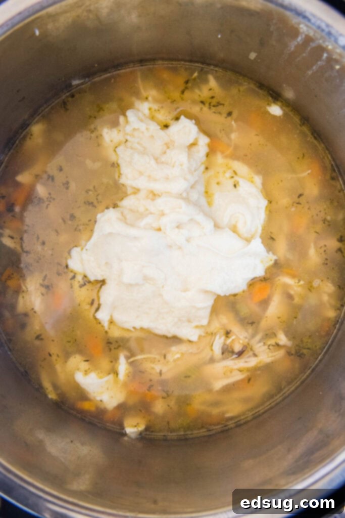 Hearty Instant Pot Chicken Wild Rice Soup 5 A hand adding a creamy roux from a saucepan into a pot of Instant Pot Chicken Wild Rice Soup