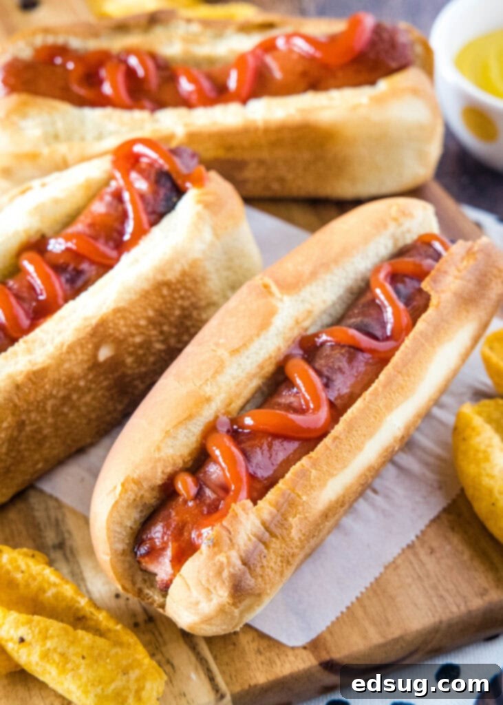 Perfect Air Fryer Hot Dogs 4 hot dogs topped with ketchup in a bun on a cutting board